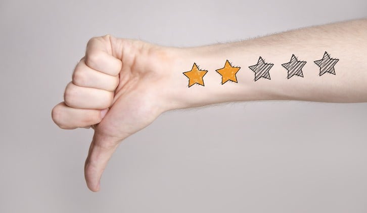 Mans hand showing thumb down and two star rating tattoo like drawing on gray background, internet rating concept