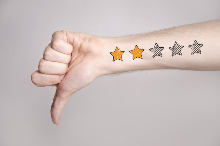 Mans hand showing thumb down and two star rating tattoo like drawing on gray background, internet rating concept