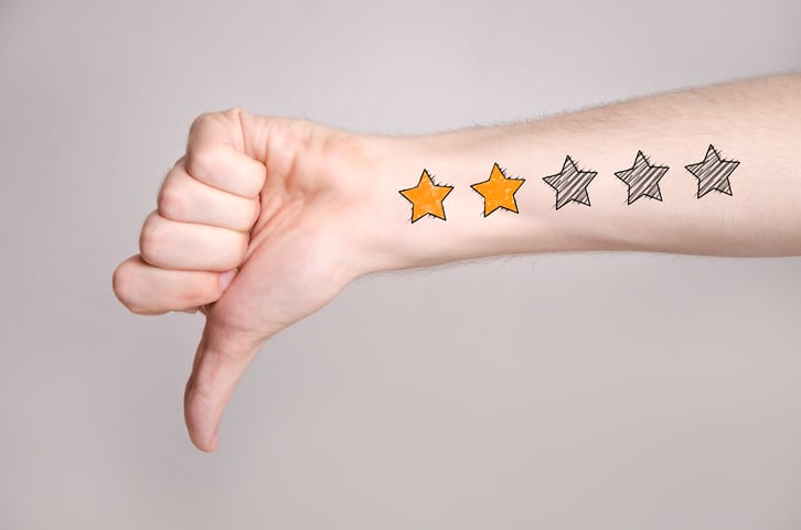 Mans hand showing thumb down and two star rating tattoo like drawing on gray background, internet rating concept