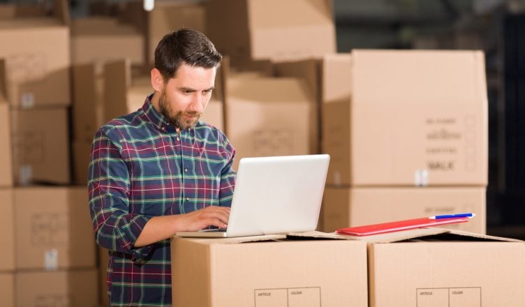 delivery manager working with laptop in a warehouse surrounded by packages