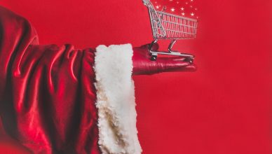 Santa Claus hand with little shopping trolley cart with stars on the red background