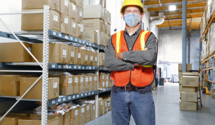 supply chain manager with face mask stands with his arms folded