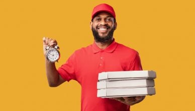 On-time delivery: Delivering Pizza On-Time Holding Boxes And Clock Smiling To Camera Posing Over Yellow Studio Background.