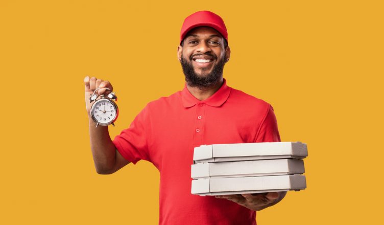 On-time delivery: Delivering Pizza On-Time Holding Boxes And Clock Smiling To Camera Posing Over Yellow Studio Background.