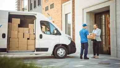 Delivery Man Gives Postal Package to a Business Customer, Who Signs Electronic Signature POD Device. In Stylish Modern Urban Office Area Courier Delivers Cardboard Box Parcel to a Man: example of how to reduce last-mile delivery costs