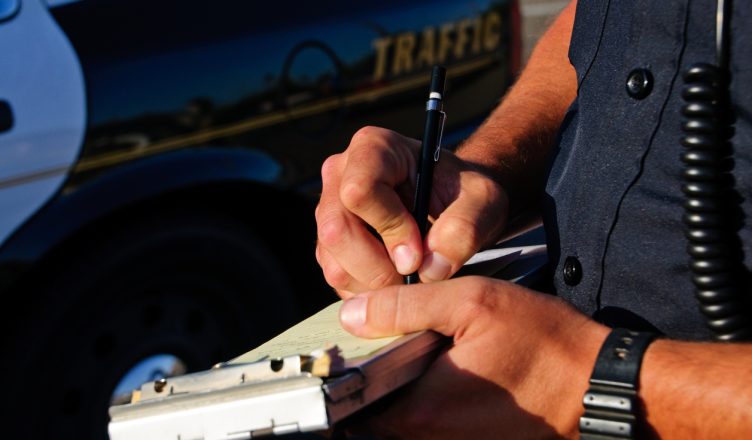 A police office on the side of the road as he writes a ticket for not adhering to DOT compliance.