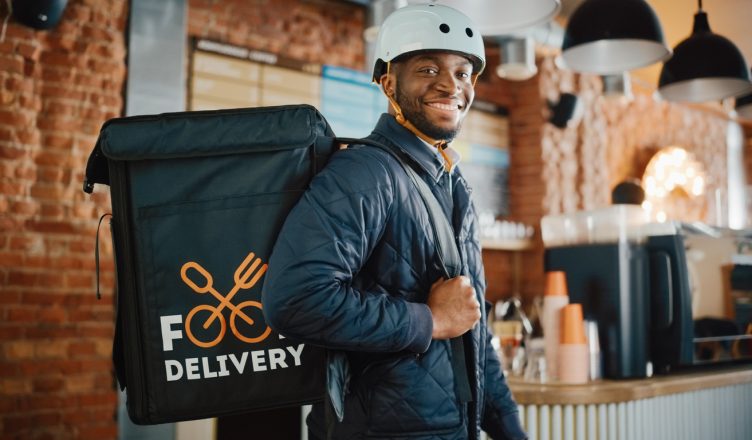 Happy and Smiling Man Wearing a Bicycle Helmet and Thermal Insulated Bag for Food on His Back to offer food deliveries services for restaurants,