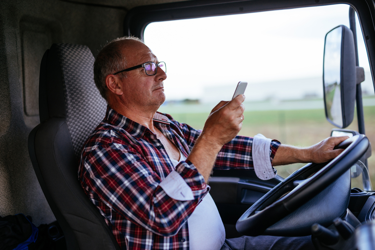 Senior man driving a truck and texting on a mobile phone.