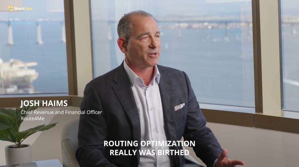Josh Haims, CFO of Route4Me, speaking in an office with a bay view behind him, discussing the origins of routing optimization.