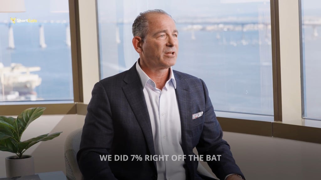 Josh Haims, CRO of Route4Me, in a suit speaking in an office with a waterfront view. Caption reads: “WE DID 7% RIGHT OFF THE BAT.”