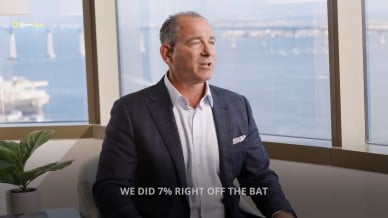 Josh Haims, CRO of Route4Me, in a suit speaking in an office with a waterfront view. Caption reads: “WE DID 7% RIGHT OFF THE BAT.”